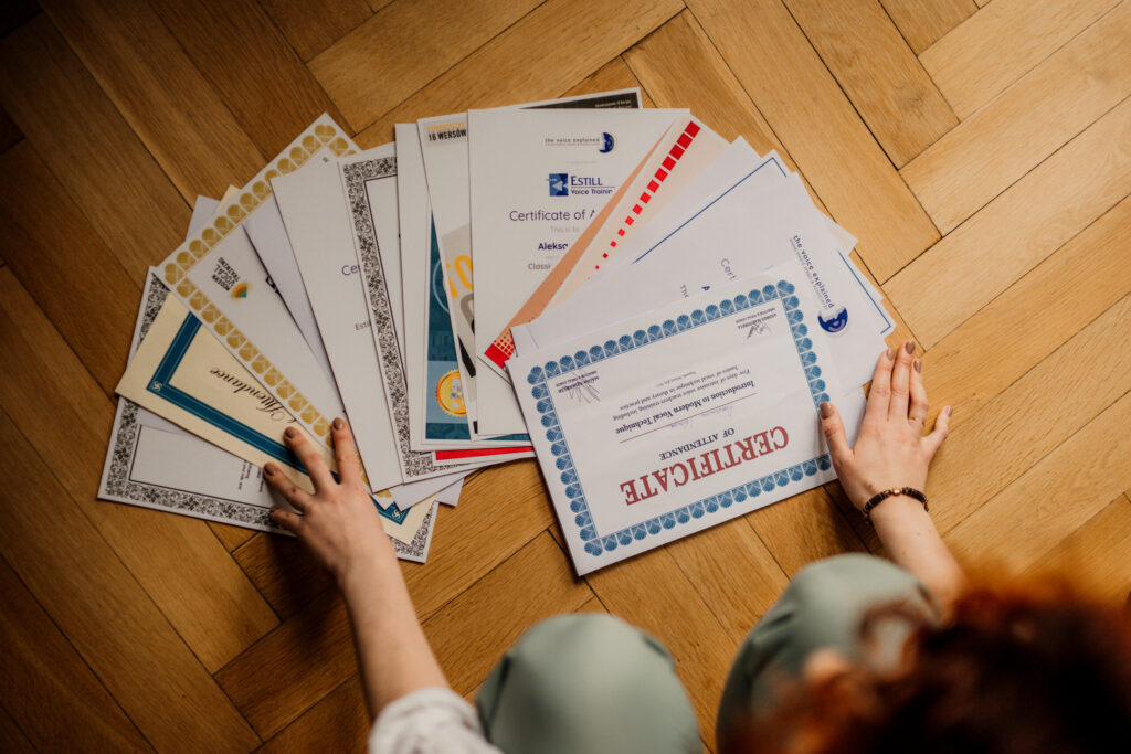 Over 20 Singing Certificates laid on a floor - Estill Voice Training, Modern Vocal Coaching, Vocology in Practice, Vocal Process that Aleksandra Vocal Coach attended.