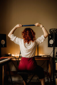 Redheaded Singer and Vocal Coach showing a singing technique with her arms up in the air flexing an exercise band in a masterclass situation in her home studio.